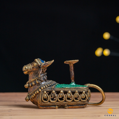 Handcrafted Nandi, the sacred bull, is intricately detailed using the ancient Dhokra technique—a method of non-ferrous metal casting practiced for centuries. The result is a stunning candle holder that not only radiates warm, flickering light but also pays homage to Indian heritage.